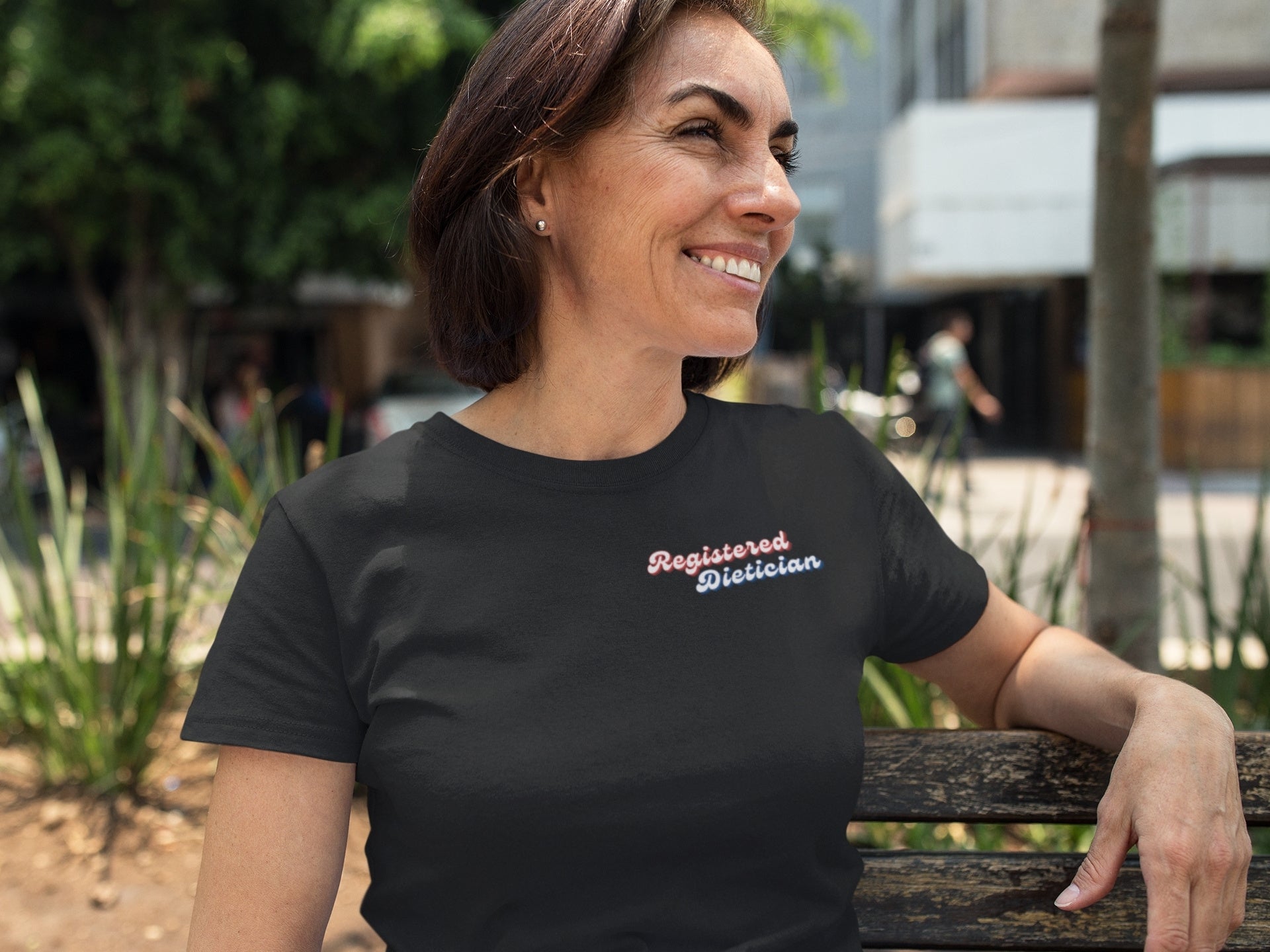 Woman wearing a black t-shirt with 'Registered Dietician' text, sitting outdoors.